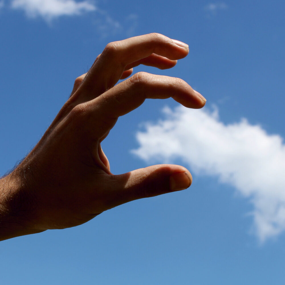 Image 1: A hand acting as if it can grasp a cloud in the sky, shot from an angle to make it look real.