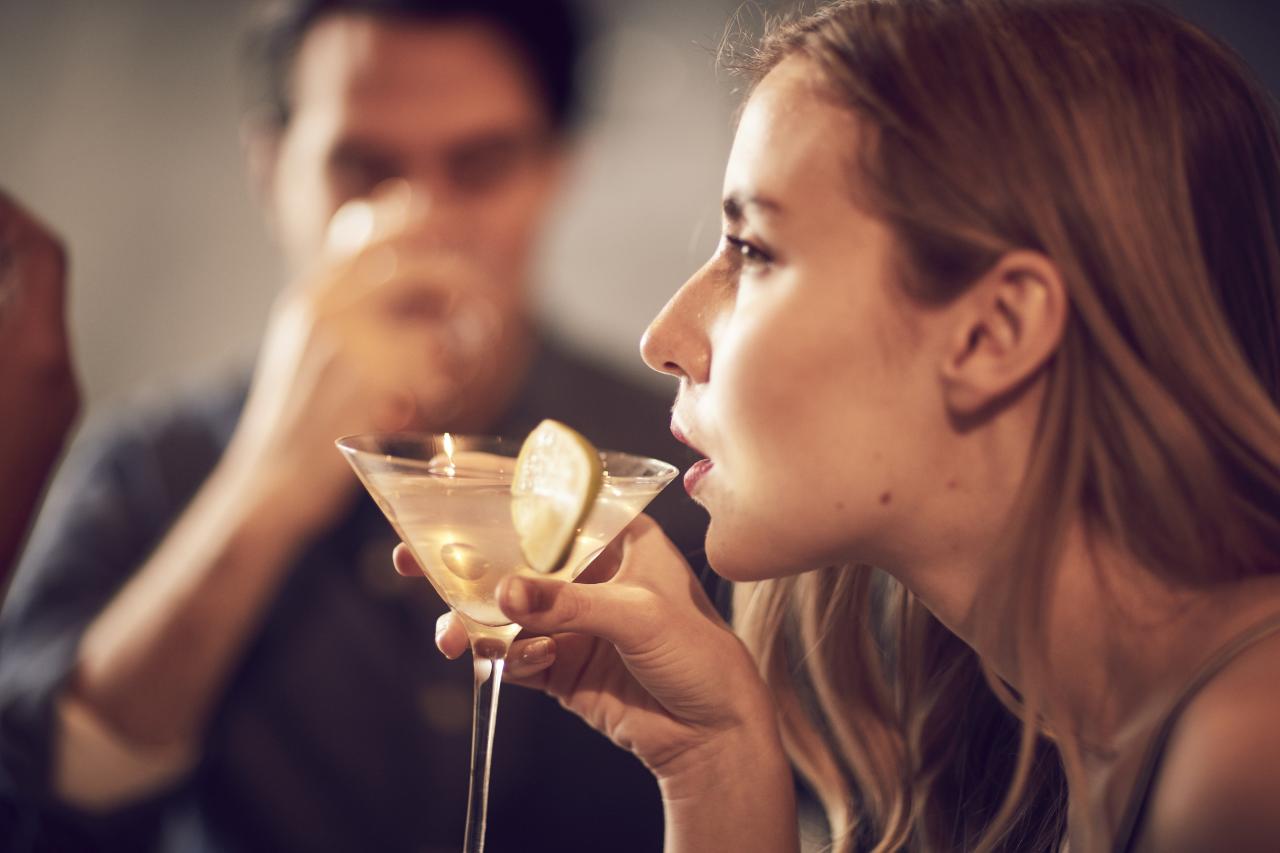 图片 44：一名女子在社交活动中从马提尼酒杯中啜饮鸡尾酒，背景中一名男子模糊